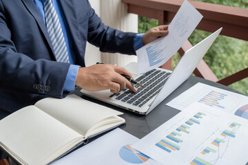 Businessman hand holding pen, analysis the graph with laptop at the home office for setting...