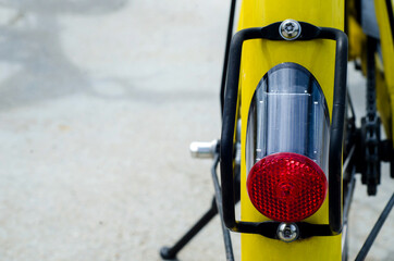 Closeup red lamp of yellow bicycle still in public garden