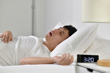 Young Asian man sleeping and snoring loudly lying in the bed. - 450606693