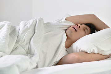 Young Asian man sleeping and snoring loudly lying in the bed.
