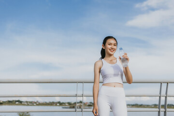 Young Asian beautiful woman drinking water during workout, running, jogging, yoga at outdoor park, fresh, relax, happy feeling. Woman fitness outdoor concept
