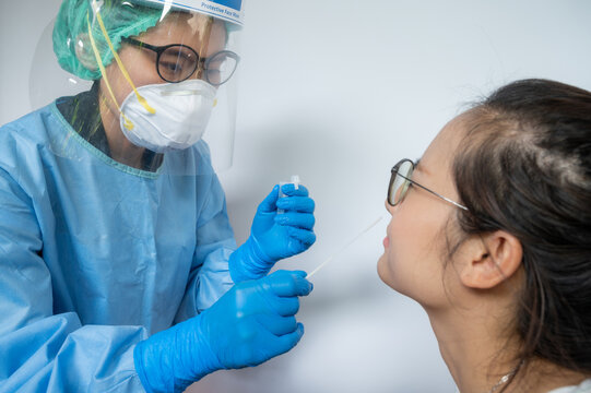 Healthcare worker trying to taking a nasal swab from Asian woman for testing diagnosis of covid-19 infection.