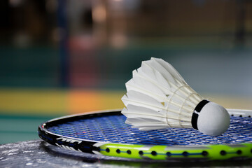 Cream white badminton shuttlecock and racket with neon light shading on green floor in indoor badminton court, blurred badminton  background, copy space. - obrazy, fototapety, plakaty