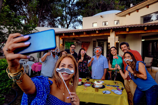 Multi generation group of latinx, latino, Latina, Mexican family and friends celebrating, props, taking a selfie with a smartphone
