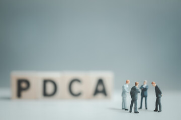A group of businessmen meeting and standing in front of blur of PDCA letters by wooden block word.