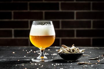 pour beer into a tall glass with a thick foam, dried fish on wooden background. Beer brewery concept. Snack for beer dried smelts. Beer background