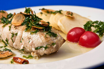 Steamed fish fillet with roasted parsley and garlic bathed in olive oil and potato slices, blue background