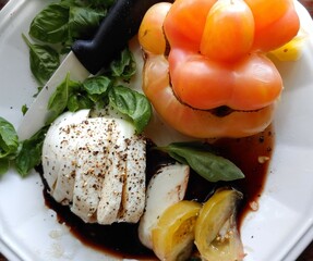 Mozzarella cheese with cracked pepper, heirloom tomatoes, basil and balsamic vinegar on a summer plate. 