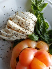 Mozzarella cheese with cracked pepper, heirloom tomatoes, basil and balsamic vinegar on a summer plate. 