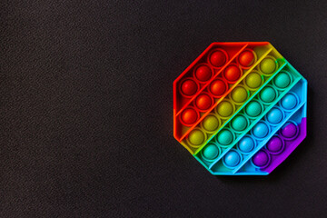 Trendy Pop it fidget toy on black background with copy space. Rainbow octagon anti stress fidget.
