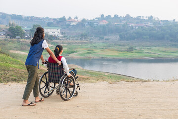 Obraz premium Disabled handicapped woman in wheelchair walking with his care helper in park.