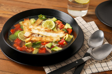 Bowl of tasty Sopa de Lima soup on wooden background