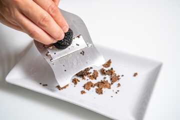 Hand slice Black truffle with truffle slicer on white background. Delicacy exclusive truffle mushroom.