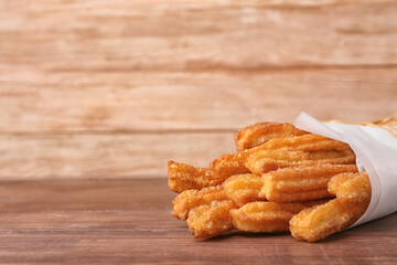 Tasty churros in parchment on wooden background, closeup
