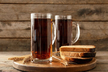 Mugs of fresh kvass and bread on wooden background