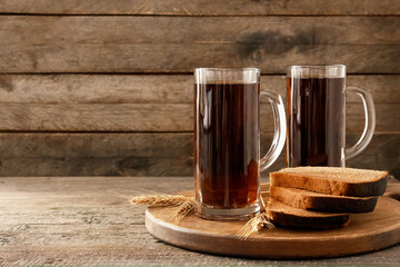 Mugs of fresh kvass and bread on wooden background
