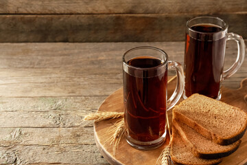 Mugs of fresh kvass and bread on wooden background