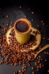 Obraz premium Coffee mugs made from bamboo on wooden saucer and many roasted coffee bean scattered on black background, dark coffee has smoke and aroma, Drink for break, morning and coffee time, local style.