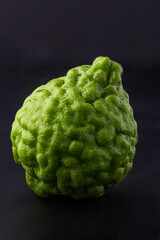 1 bergamot isolated on dark background, There are many names such as Kaffir lime, Leech lime and Mauritius papeda. it's green, rough, sour and aroma. Herbs for cooking and medicine. - obrazy, fototapety, plakaty