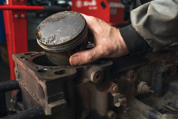 An auto mechanic shows a worn out engine piston with a deformation on the head - obrazy, fototapety, plakaty