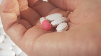 A sick person shows on the palm of his hand two white tablets and a pink capsule that the doctor prescribed for him. Against the background of a hospital white floor on a sunny day. 