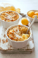 Dessert crumble with apricots, ricotta and coconut chips in white ceramic bowls close up