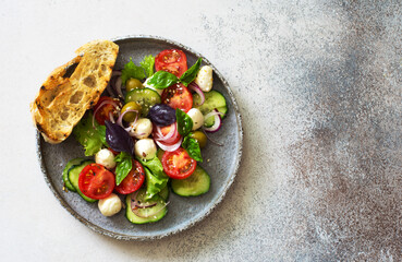 Plate of raw vegetable salad with tomatoes, cucumbers, mozzarella and greens
