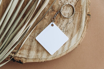 Keychain mockup among brown palm leaves to display design. Blank white sublimation key chain photo.