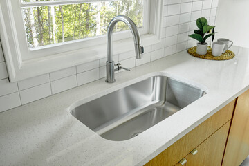 stainless steel faucet and sink. white countertops with brown cabinets