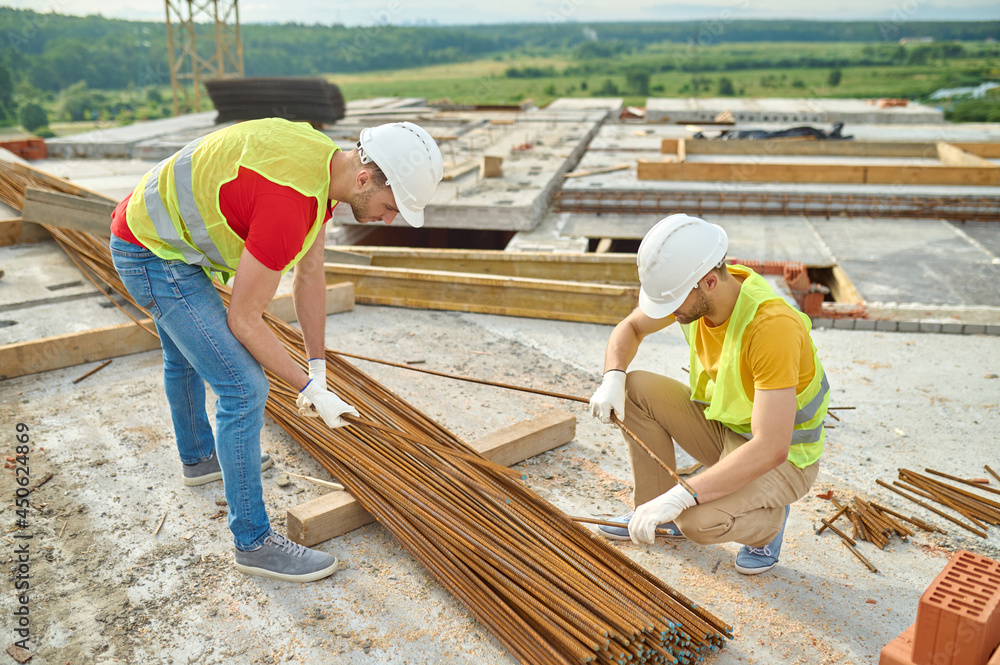 Poster Experienced focused builders in cotton gloves selecting rebars