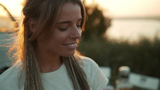 A happy woman is looking to the camera standing near caravan trailer outside