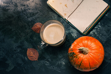 One pumpkin squash and a latte coffee made with with plant based oat soya or almond milk  with blank notepad notebook at the table on the dark black blue textured copy space background work concept
