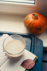 One pumpkin squash and a latte coffee made with with plant based oat soya or almond milk  with blank notepad notebook at the table on the dark black blue textured copy space background 