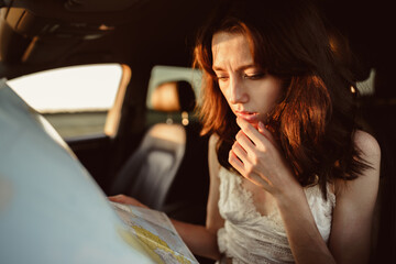 Lost young woman sitting in her car in the countryside and looking at map