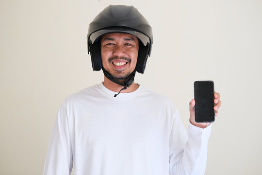 Adult Asian man wearing motorbike helmet while showing blank cellular phone screen