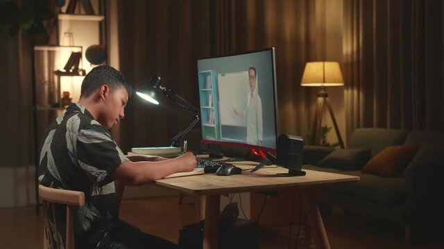 Asian Boy Student Distance Learning And Writing With Online Teacher On Computer Screen From Home
