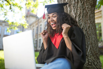 A cute graduate in academic gown having a vieo call and feeling happy