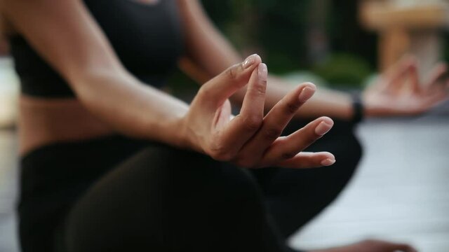 A close-up cropped view of a calm afro-american woman doing meditation holding hands in a dzen sign sitting on the yoga mat outside