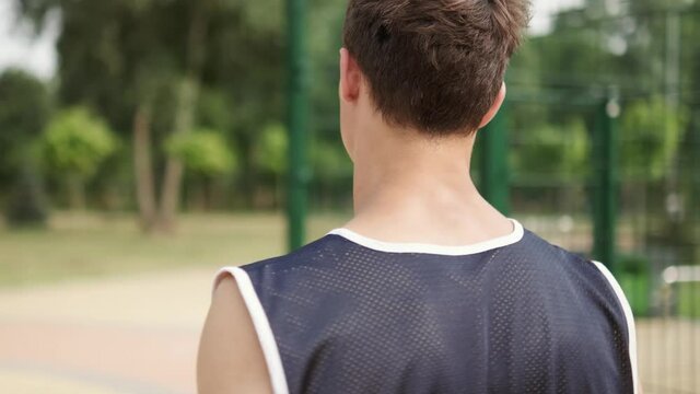 A back view of an attractive guy is coming to basketball playground outdoors