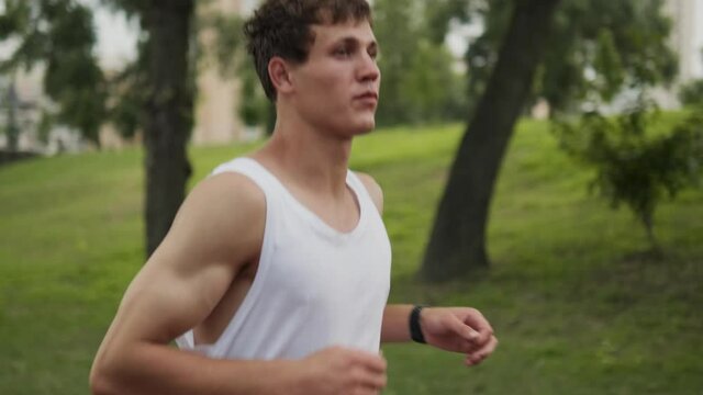 A handsome guy is running at playground outdoors while using his fitness tracker