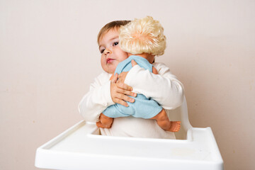 Baby toddler hugs with old-fashioned doll on a studio shot. Funny serious face. Best friend toy. Role independent play of toddler. Montessori education