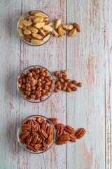 Three kinds of nuts in three glass bowls on a wooden table, healthy fat and protein food, vegan, ketogenic diet.