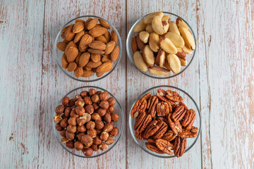 Four types of nuts in four glass bowls on a wooden table, healthy fat and protein food, vegan, ketogenic diet.