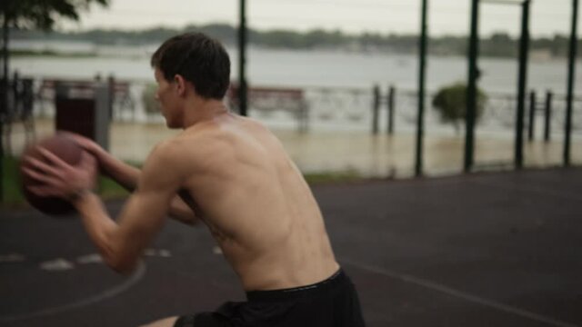 A half-naked man is playing basketball at the sports ground during rain