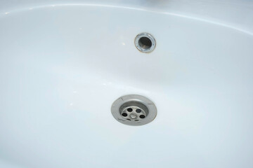 Water is dripping small drops in drain hole of the white sink in bathroom, closeup view. Danger of...
