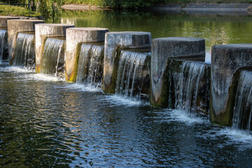 Long concrete cascade with flowing water on a river in a summer city park
