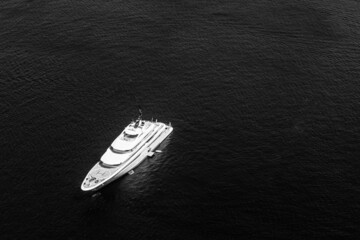 Black and white dramatic process pf aerial drone top down photo of luxury exotic yacht with wooden deck anchored in Aegean island with deep blue sea, Greece.  