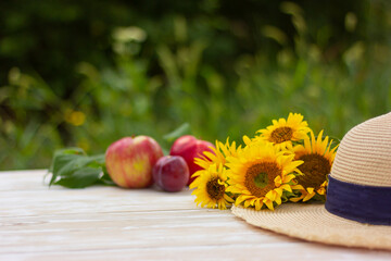 a bouquet of sunflowers and a straw hat on a background of fresh fruits on a wooden table in the...