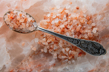 A bunch of large crystals of pink Himalayan salt on the surface of a large slab of Himalayan salt....
