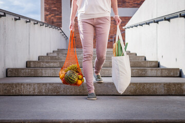Woman walking at stairs and carrying reusable mesh bag after shopping groceries in city....